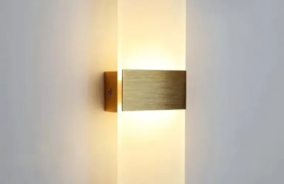 Aplică LED dreptunghiulară aurie cu difuzor acrilic aprinsă pe un perete modern